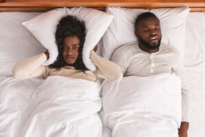 Snoring husband. Unhappy black woman covering her ears with pillow, can not handle loud snore of her partner, top view